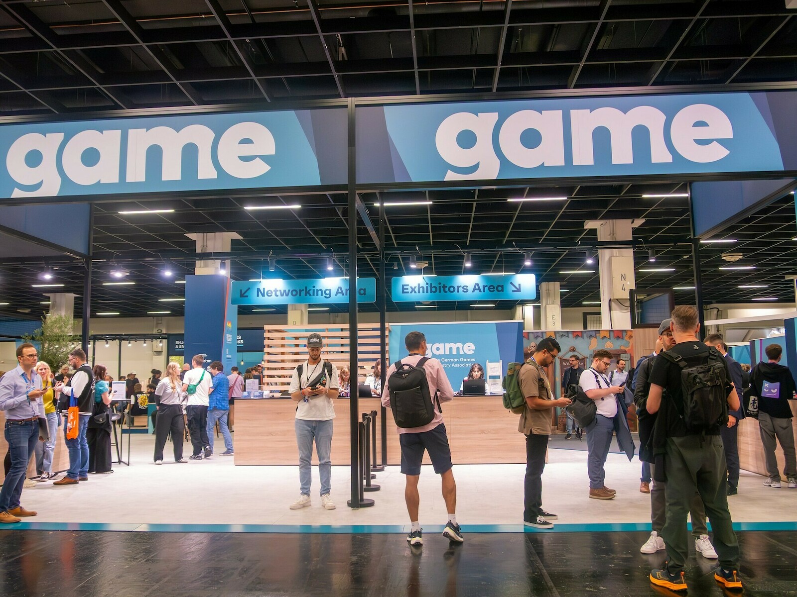 Le stand de l’association game dans un hall de la gamescom, des visiteurs devant l’entrée